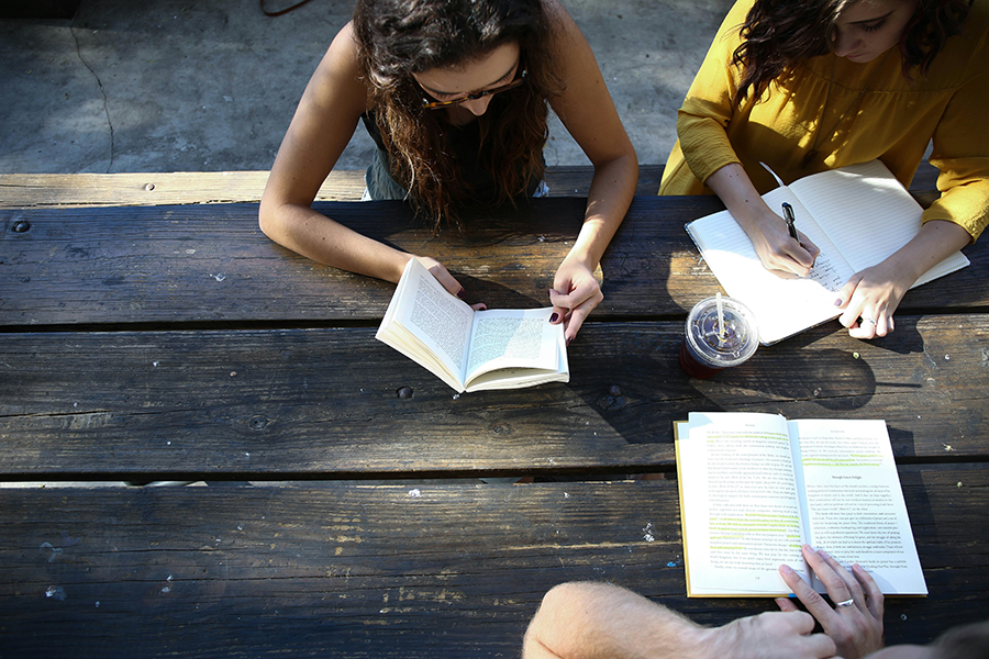 Three people sitting at a picnic table reading