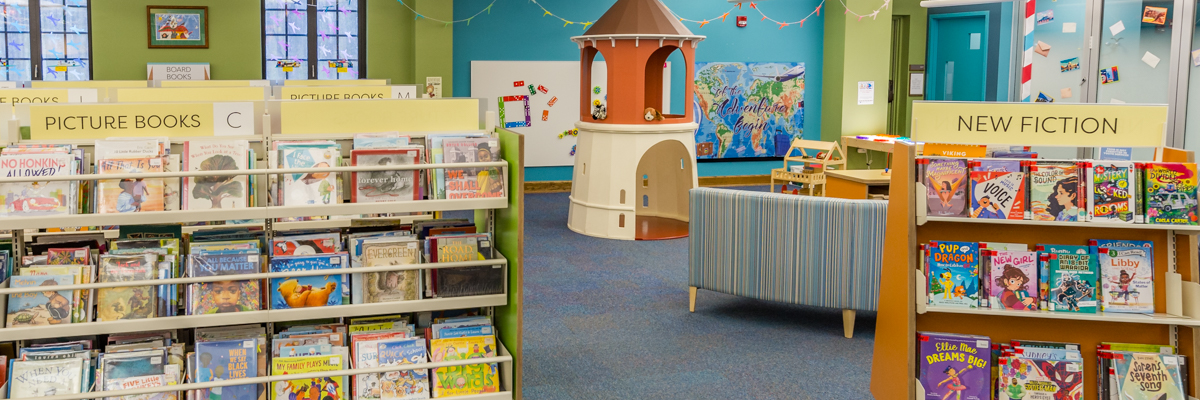 Library's children's area featuring labelled shelves, comfy seating, play tower, and wall play stations