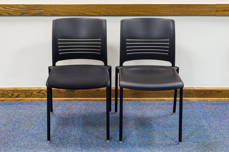 Two black chairs (one padded and one not) against a wall