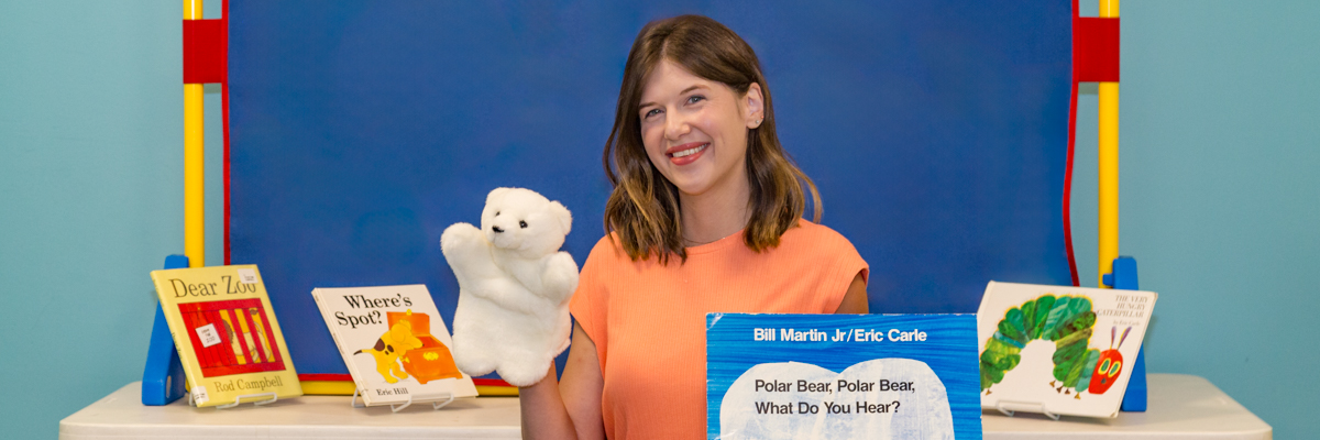 Librarian smiling with puppet and children's books