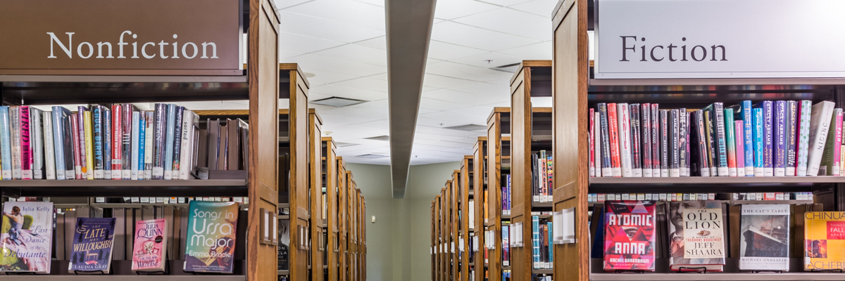 Perspective shot down library aisle of wooden shelving with "Nonfiction" and "Fiction" signs over each side