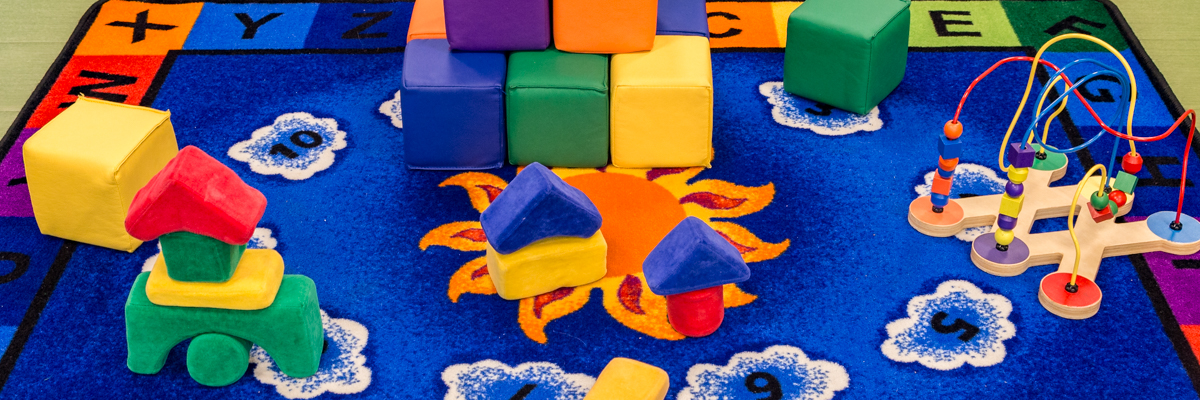 Close up of colorful blue play area rug, big soft blocks, and bead toy