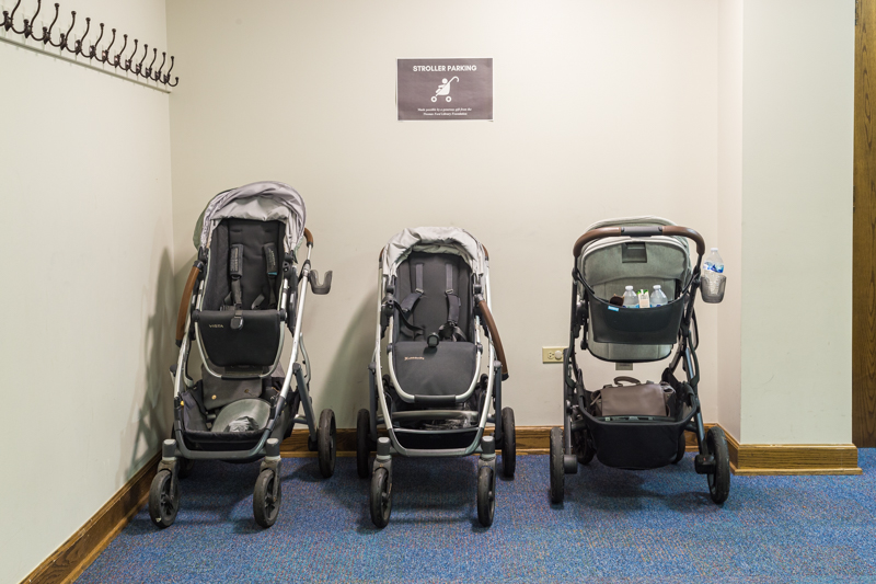 Three baby strollers parked against a wall with sign designating the area