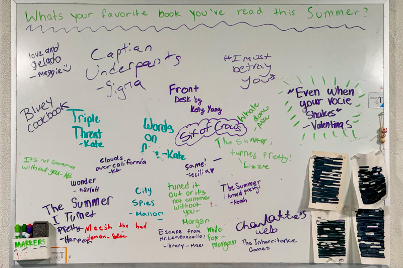 White board with "what's your favorite book you've read this summer" and hand written responses in different color markers