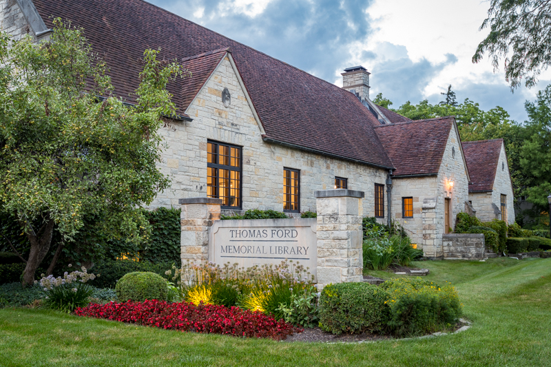 Side view of library white stone building and red roof tiles featuring outdoor name sign and landscaping